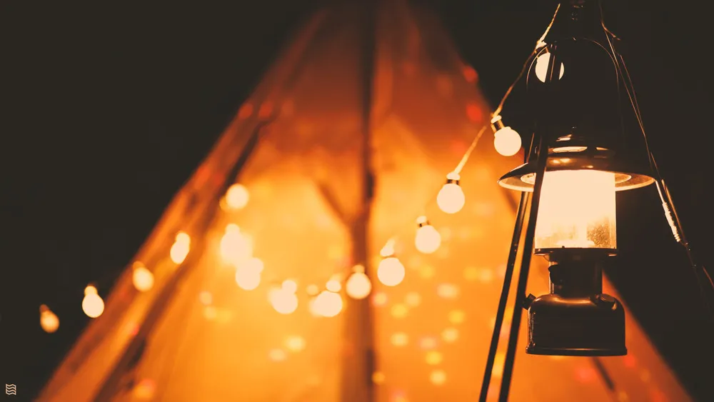 a gas lantern hanging with some light blubs hanging in the night with a tent in the background